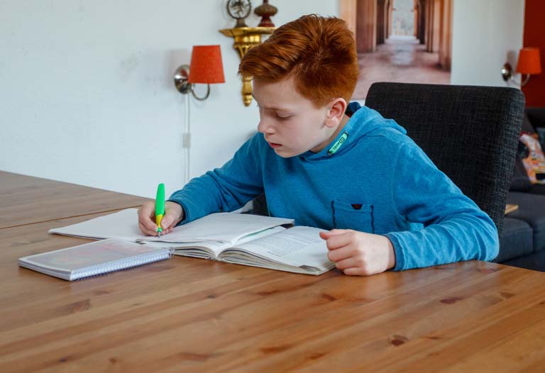 Schüler sitzt am Tisch und macht Hausaufgaben
