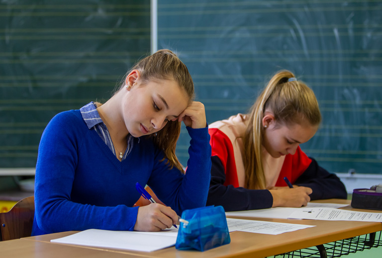 Zwei Schülerinnen arbeiten am Tisch vor einer Tafel