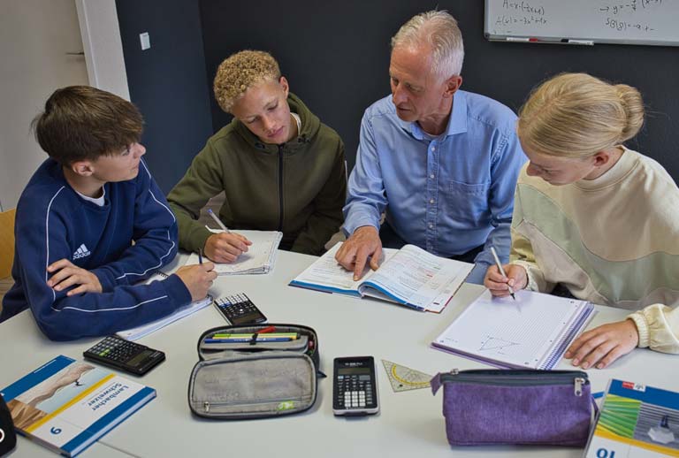 Nachhilfelehrer mit drei Schüler:innen, die Mathematik lernen.