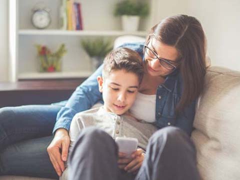 Mutter und Sohn sitzen auf der Couch und schauen auf ein Handy.