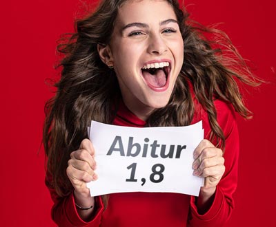Schülerin freut sich über ihre Abitur-Note und hält einen Zettel mit der Note 1,8 hoch.