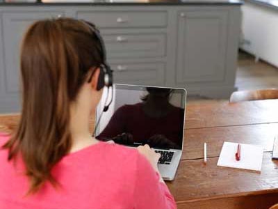 Schülerin mit Headset nimmt Online-Nachhilfe am Laptop und sitzt am Tisch.