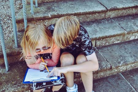 Zwei Kinder sitzen nebeneinander und schauen in ein Heft